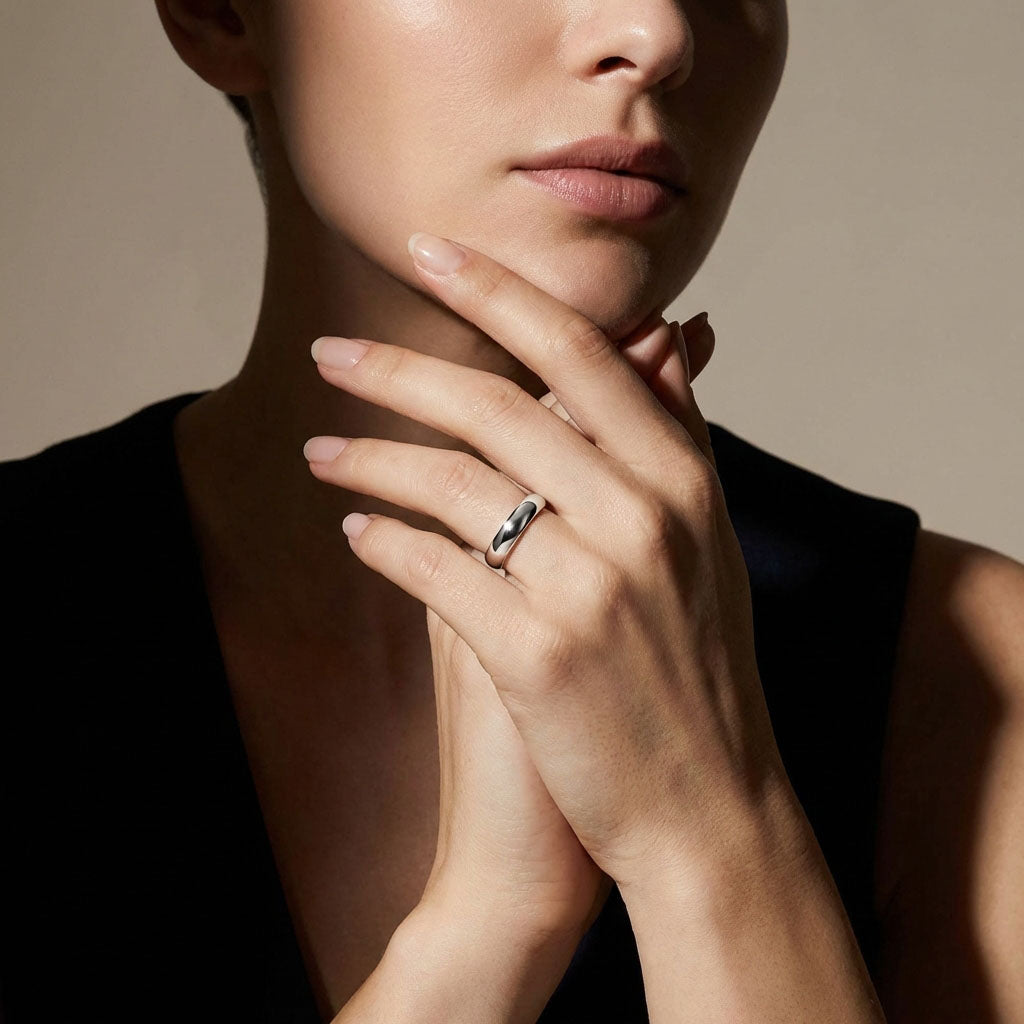 Smooth silver-tone ring on a woman's finger, hand raised to her chin