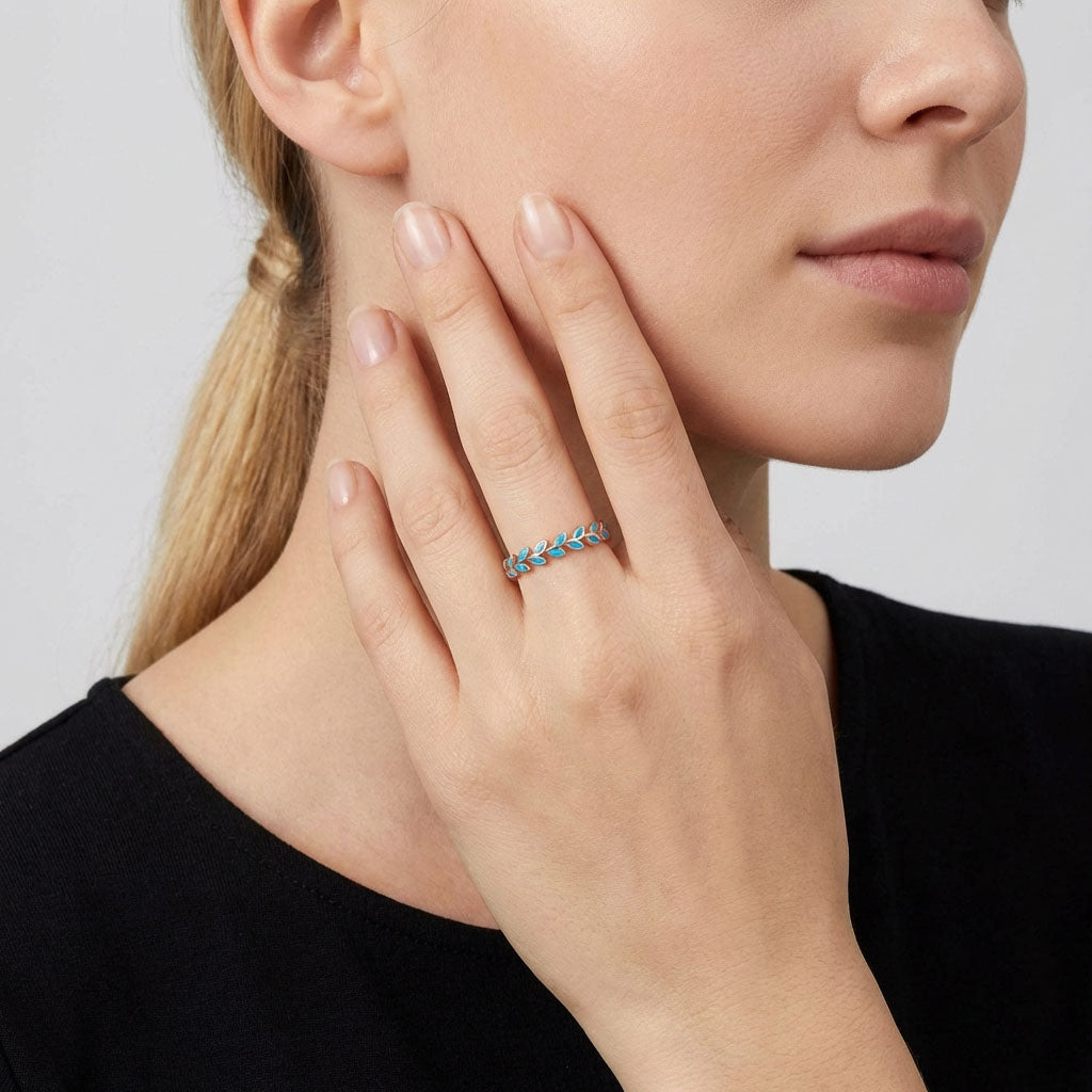 Model wearing a delicate leaf ring with turquoise enamel, hand near her face