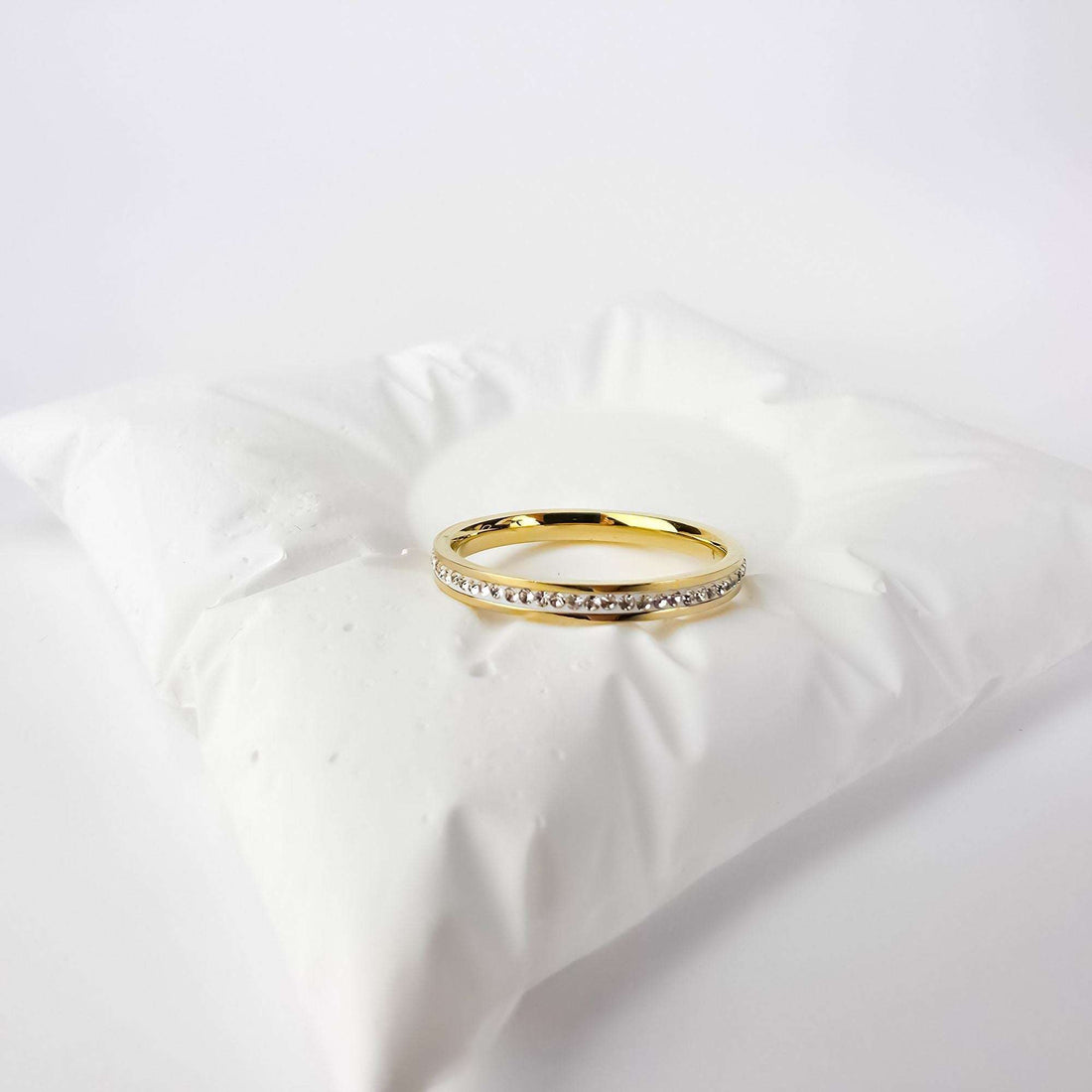 Narrow gold-plated ring with a cubic zirconia row on a white cushion