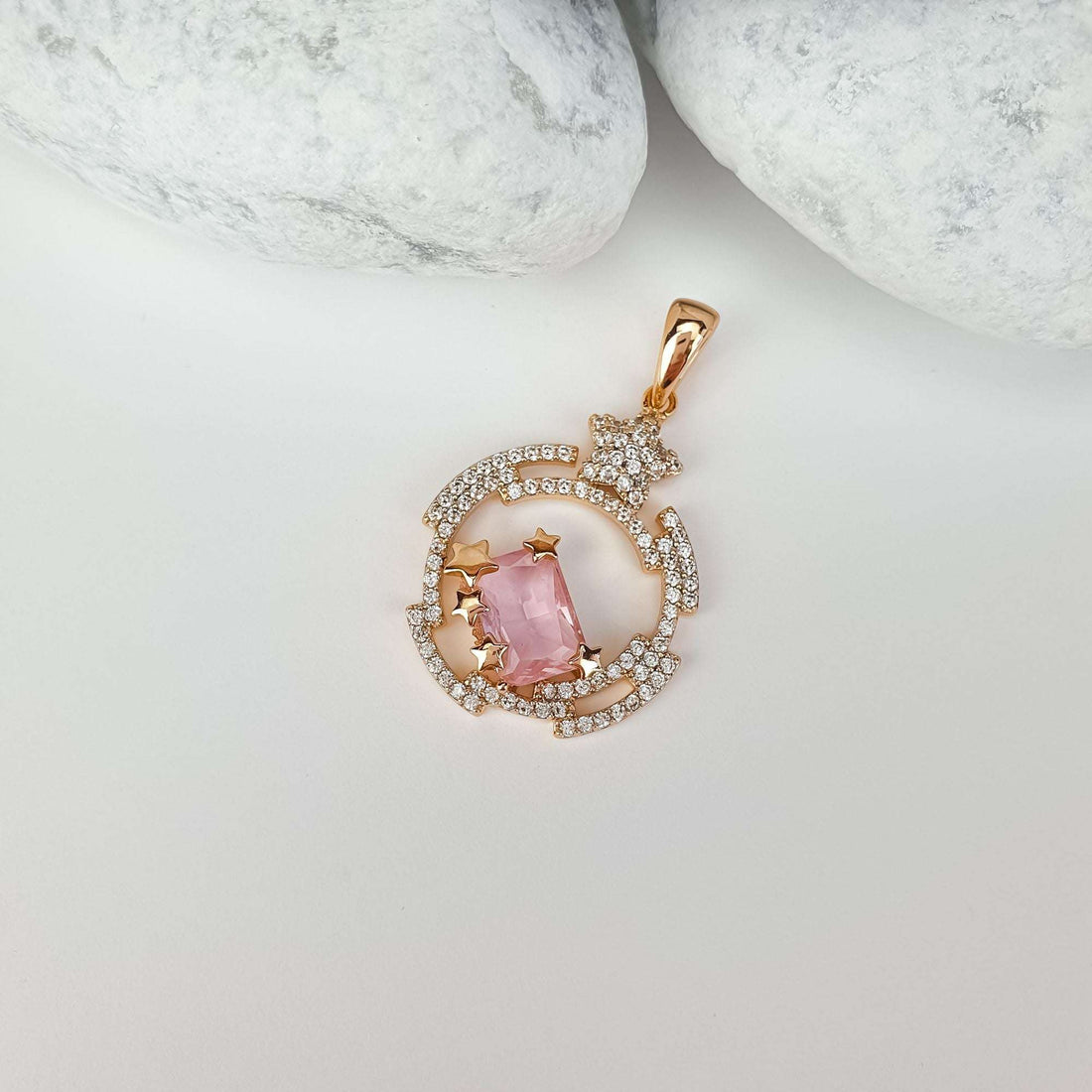 Star pendant with a pink stone on a light surface beside white pebbles