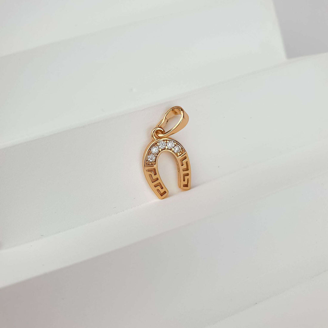 Gold-tone horseshoe pendant at an angle, bail visible, light background