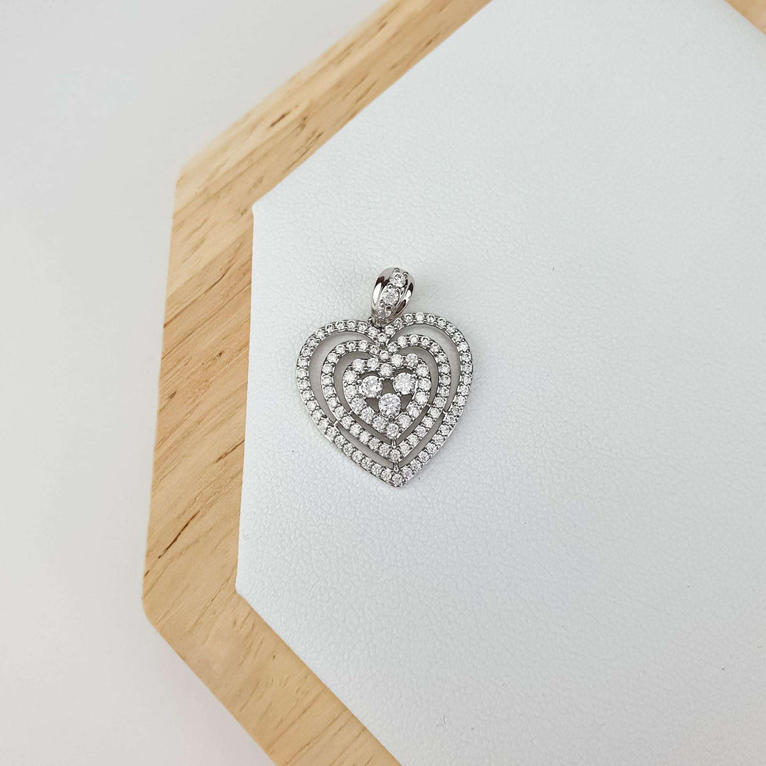 Sparkling silver-tone heart pendant on a light leather stand with a wooden edge