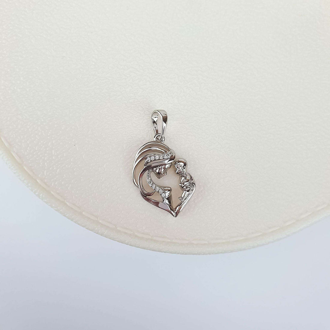 Silver-tone mother and child pendant on a cream jewellery tray, close-up