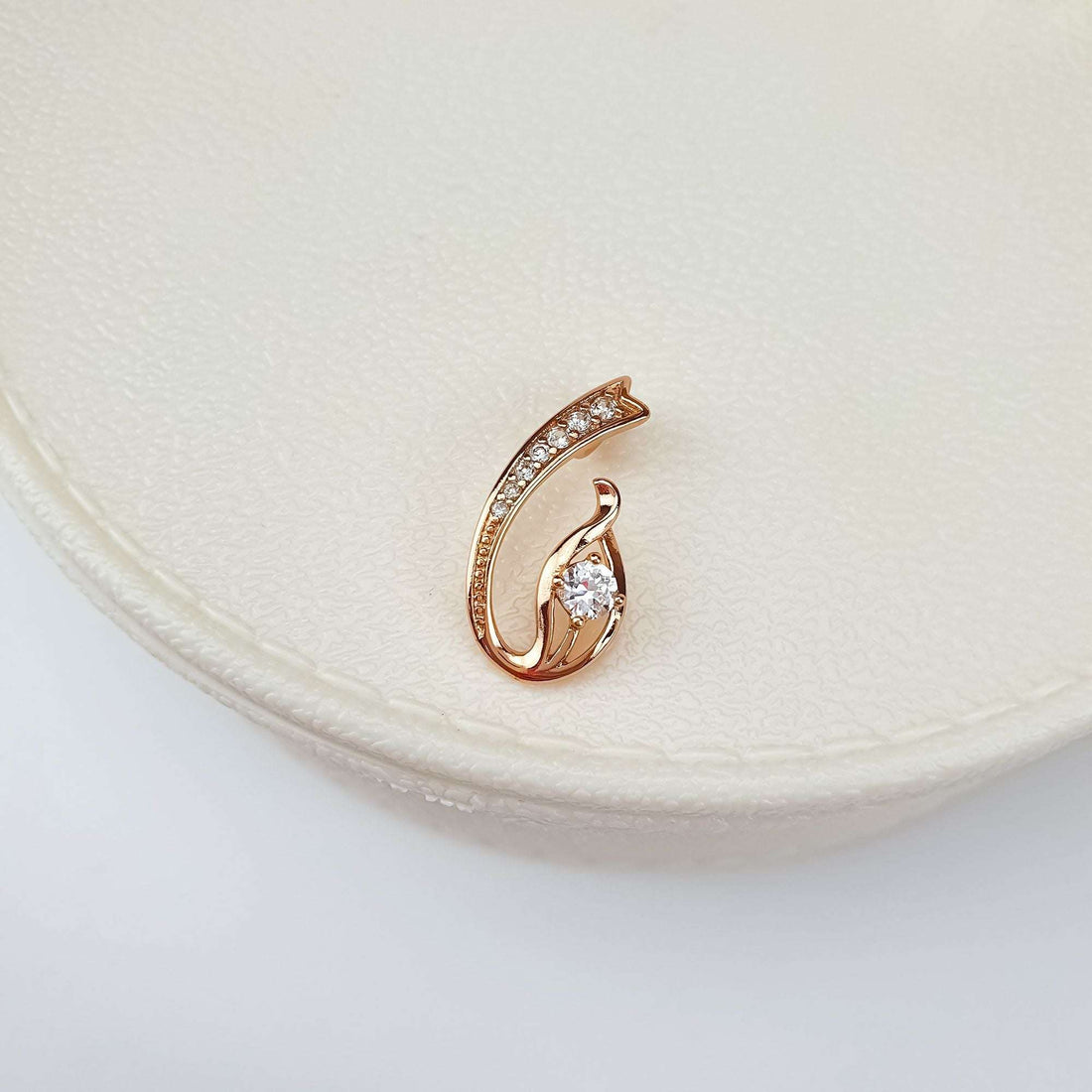 Rose-gold-tone pendant with a central cubic zirconia, close up on a cream ceramic stand