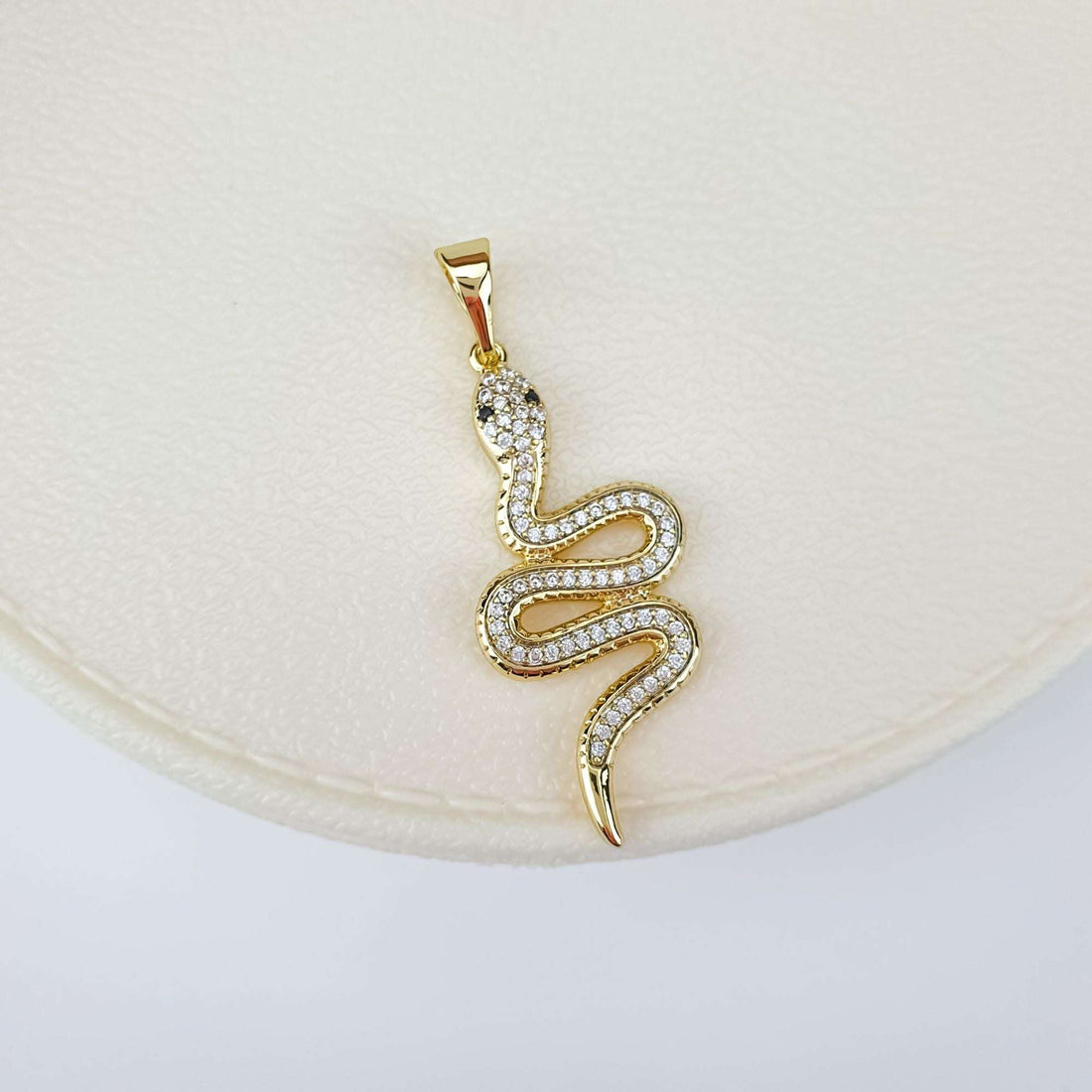 Close-up of the snake pendant's sparkling stones on a cream jewellery box