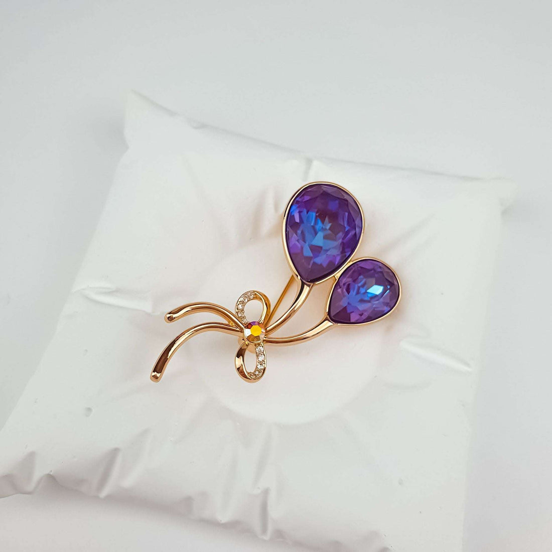 Gold-plated brooch on a white cushion, violet balloon crystals with a bluish shimmer