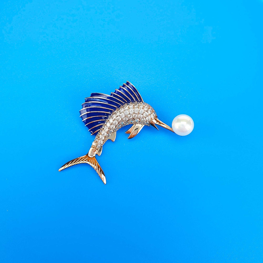 Fish brooch on a bright blue background with sparkling crystals and faux pearl