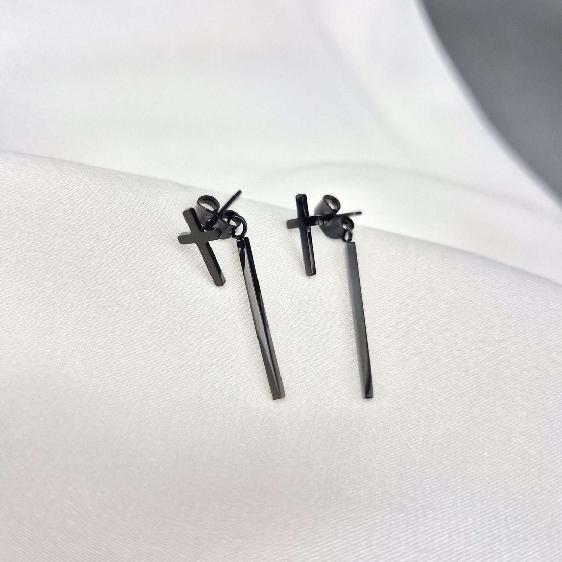 Black cross earrings with bars on white silk fabric, push-back fastenings visible