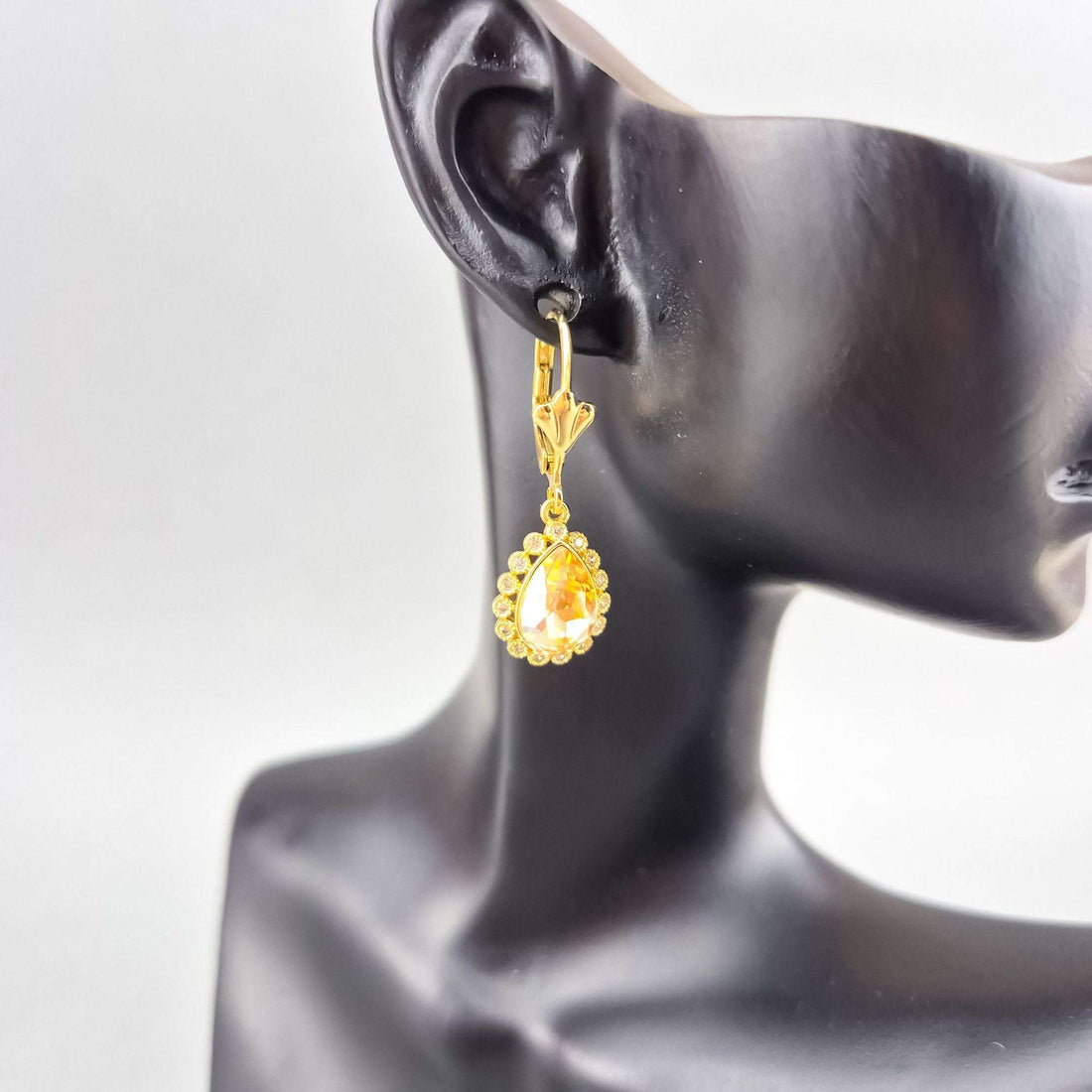 Gold-plated earring with a teardrop crystal shown on a mannequin ear