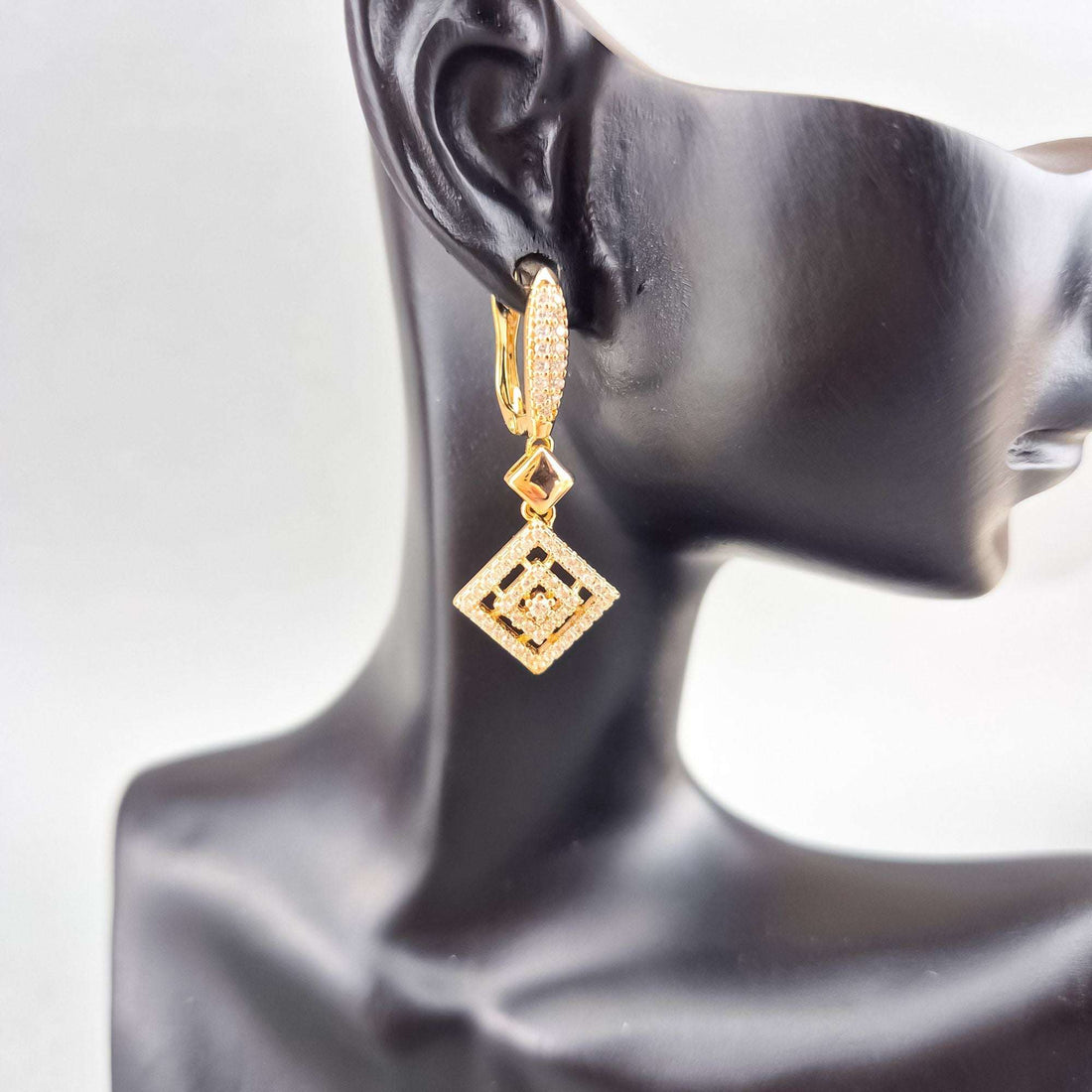 Gold-plated rhombus earrings with cubic zirconia shown on a dark mannequin ear
