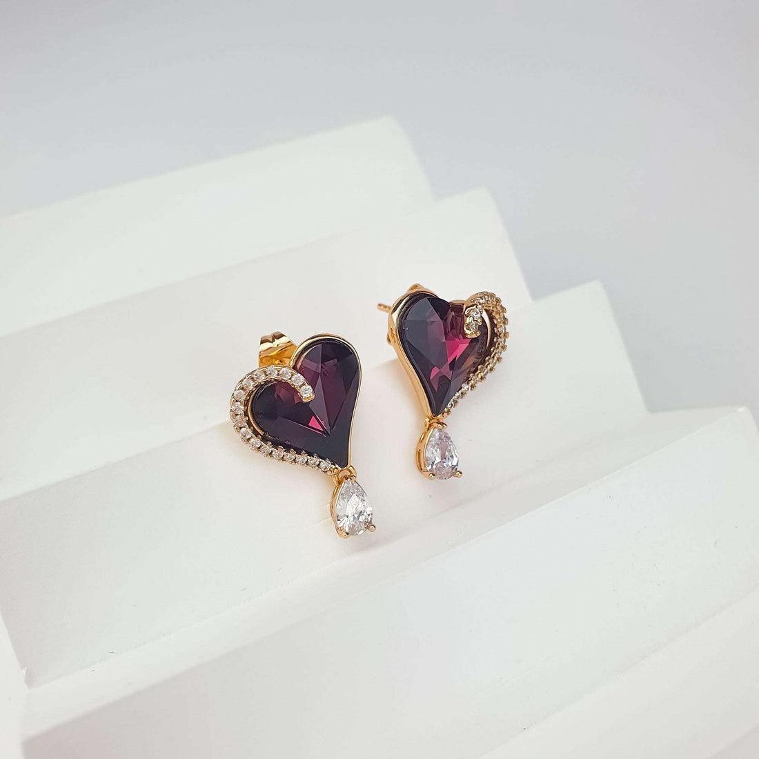 Violet crystal heart earrings angled on a white stand, push-back fastening visible