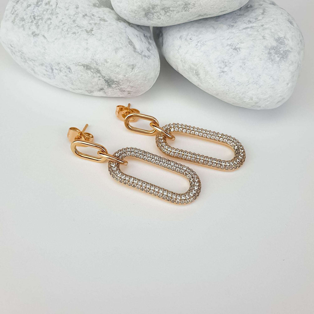Gold-tone link earrings at an angle on white stones, post fastening visible