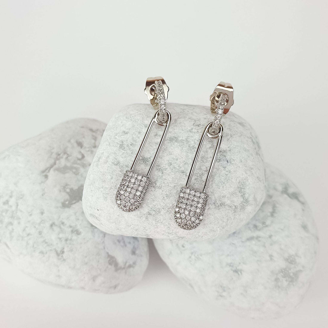 Silver-tone safety pin earrings set with cubic zirconia, at an angle on white stones