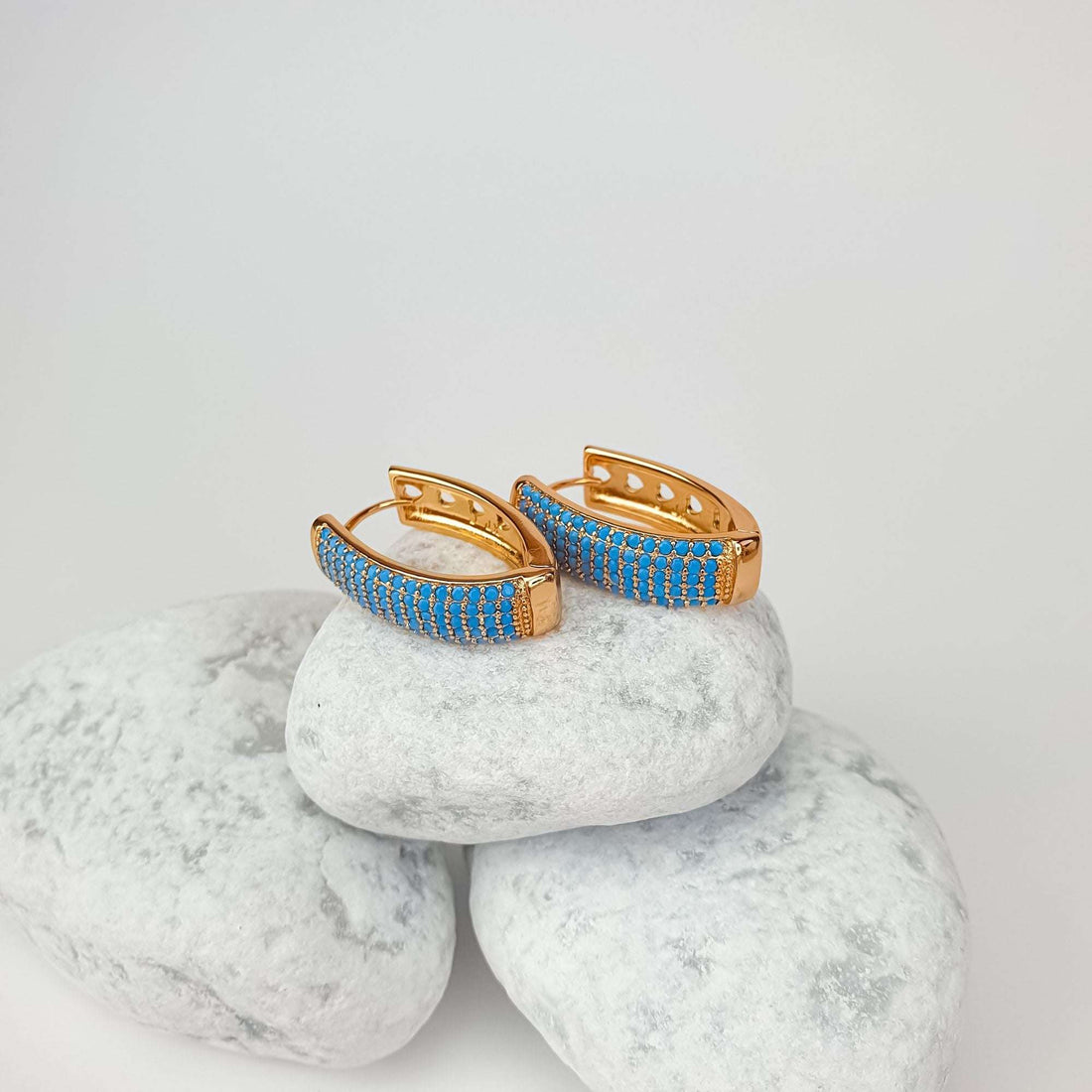 Gold-plated blue stone earrings on white pebbles, secure clasp visible