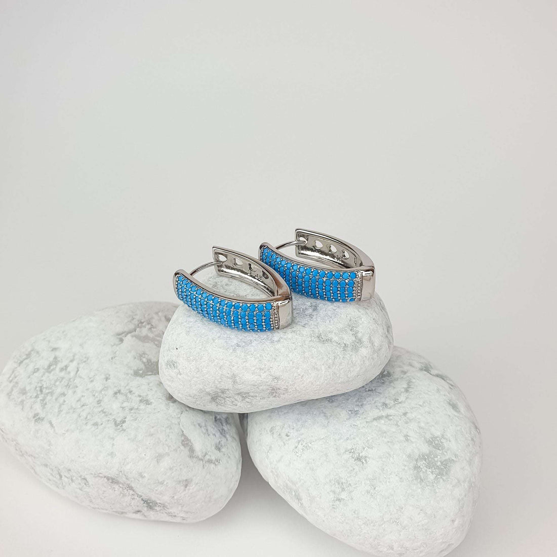Silver-tone earrings in side view with rows of blue stones on pale pebbles