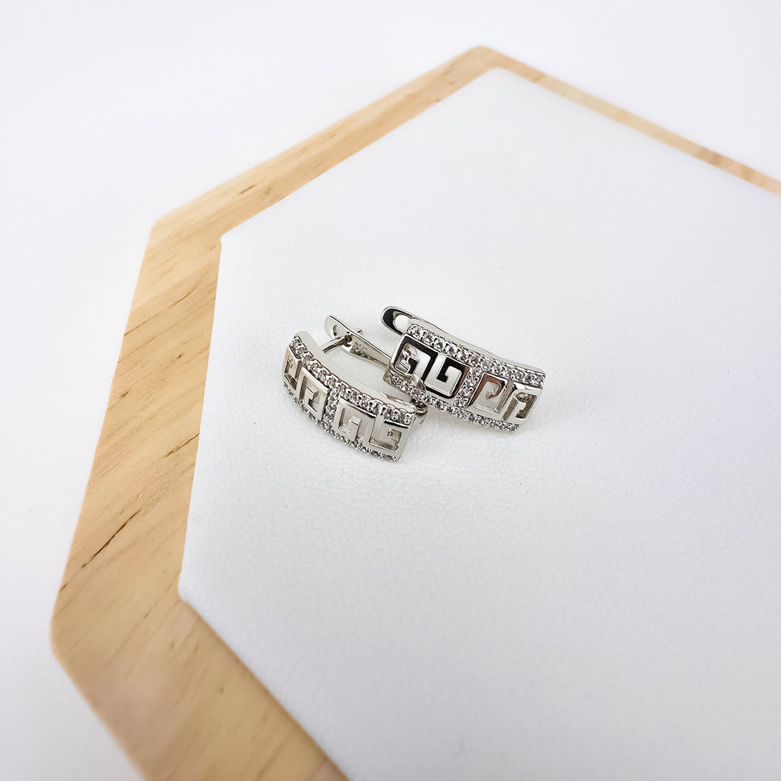 Pair of silver-tone meander earrings with leverback clasps on a wooden stand