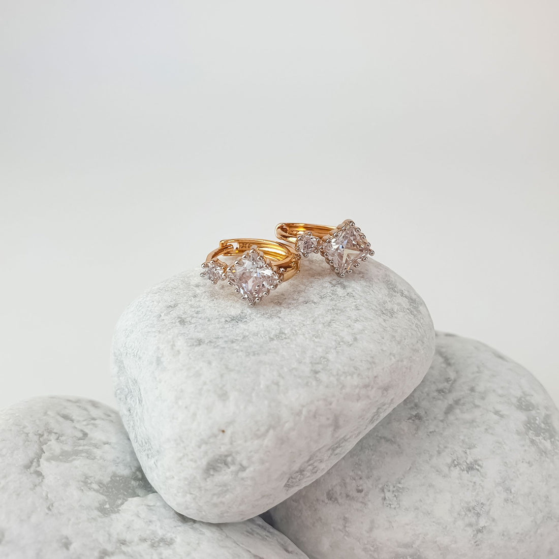 Square cubic zirconia earrings on white pebbles, gold-tone hoop closure visible