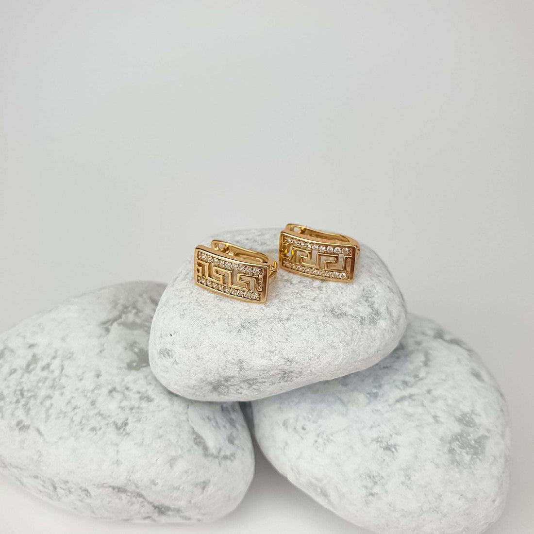 Side view of gold-tone meander earrings with cubic zirconia on white pebbles