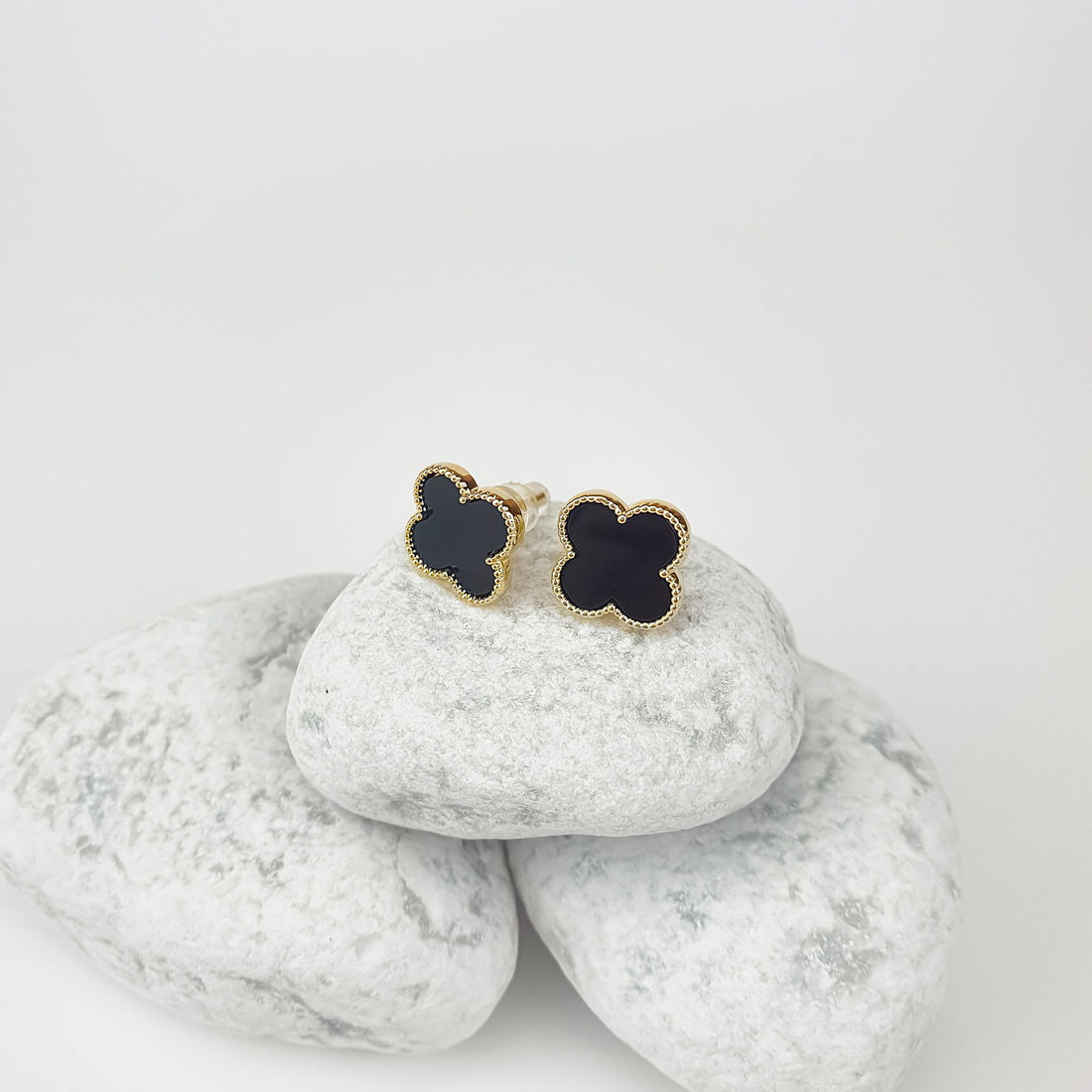 Black clover earrings on white pebbles, close-up of gold-tone rim and push-back post