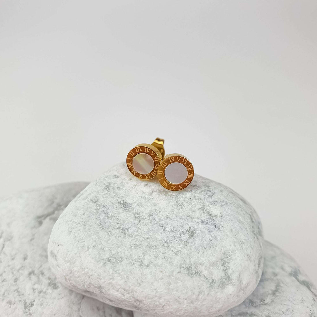Gold-tone button studs with Roman numerals and faux pearl, side view on white stone