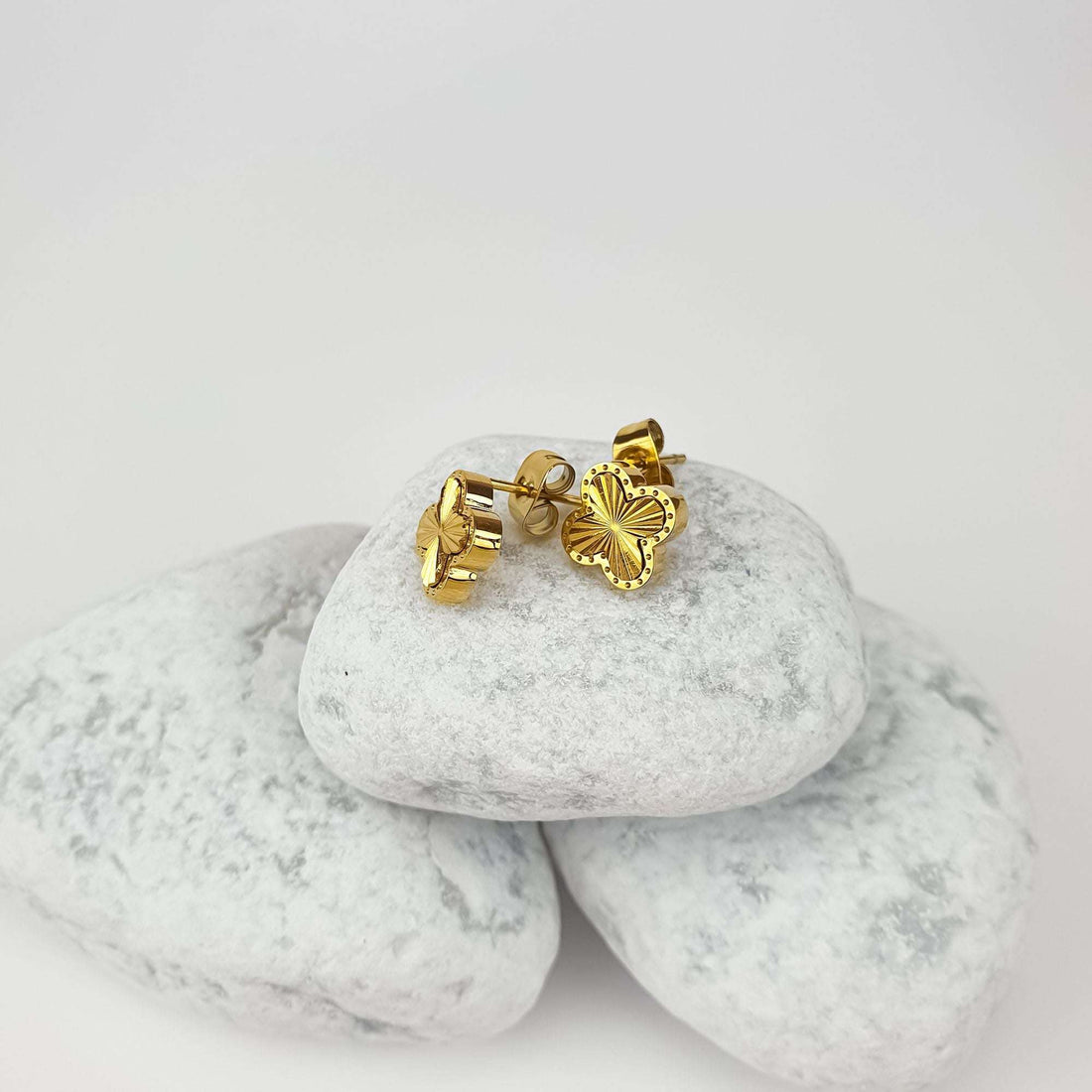 Gold-plated clover earrings on white pebbles, side view showing the push-back posts