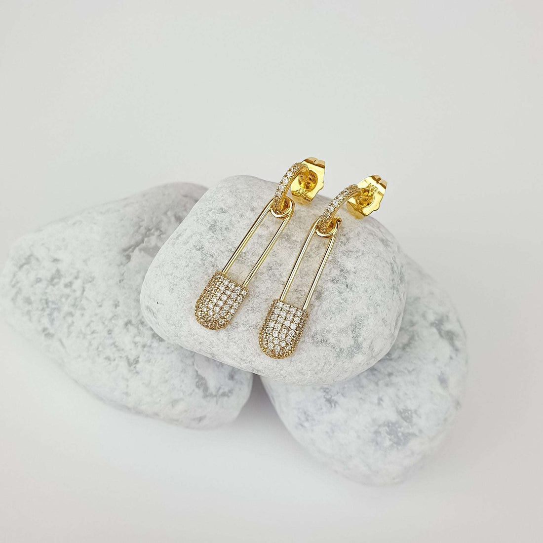 Gold-plated safety pin earrings with cubic zirconia and push-back studs on white pebbles