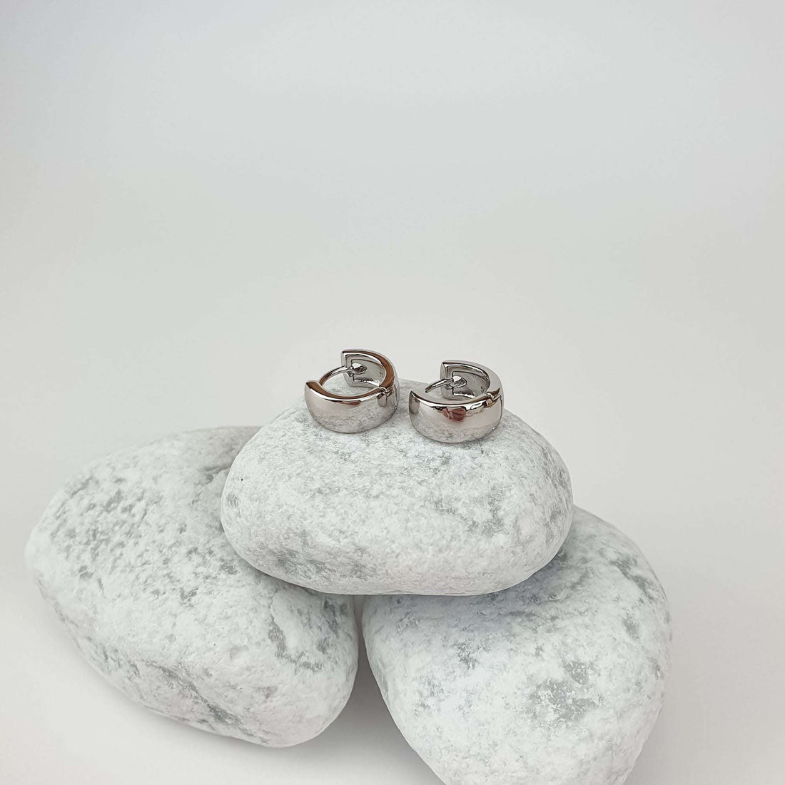 Small silver-tone hoop earrings on white pebbles, smooth clasp mechanism visible
