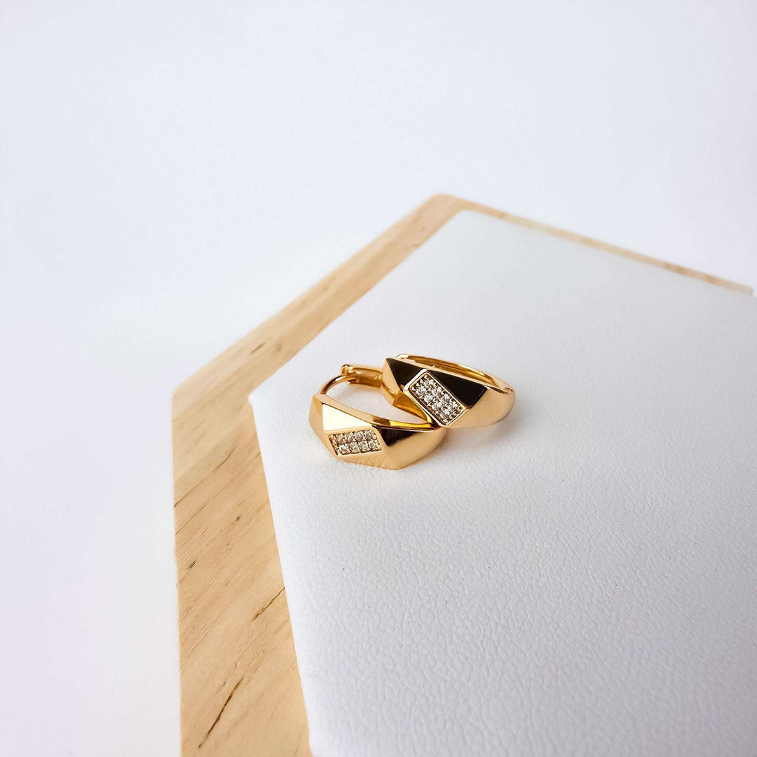 Pair of gold-plated earrings with cubic zirconia rhombuses on a white leather stand