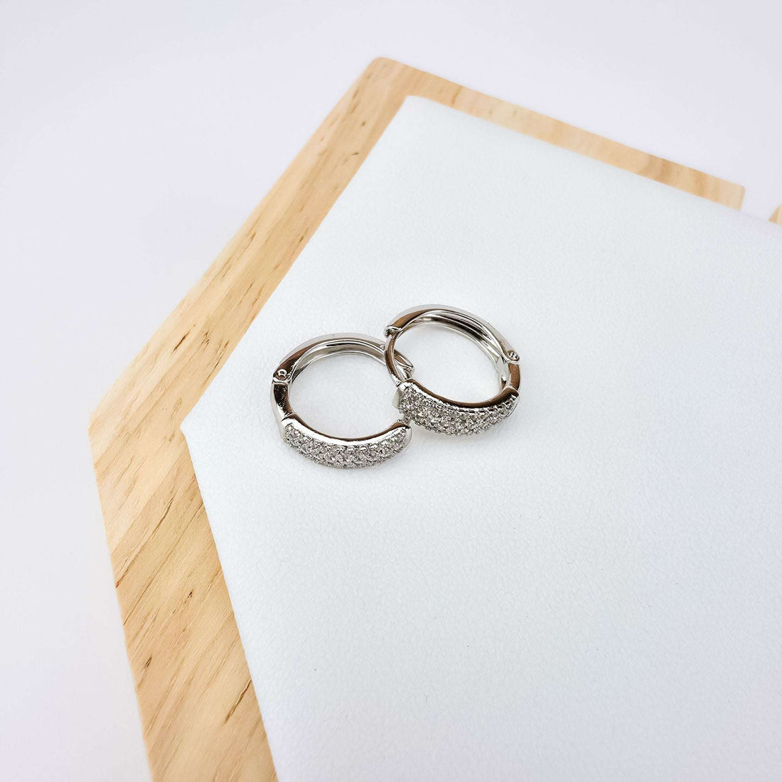 Silver-tone hoops with cubic zirconia rows on a white wood-framed tray