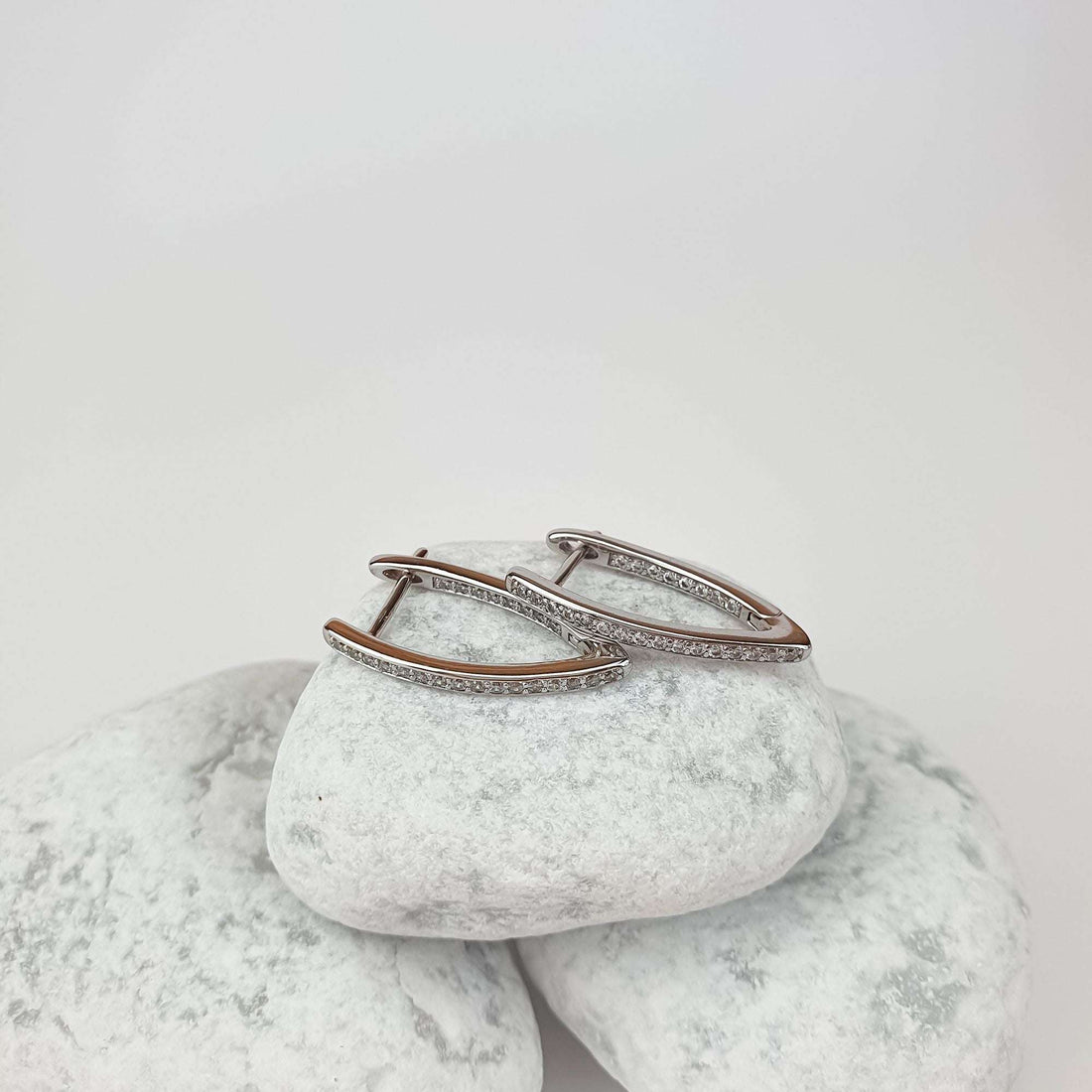 Elongated pointed hoops with a line of cubic zirconia on white pebbles