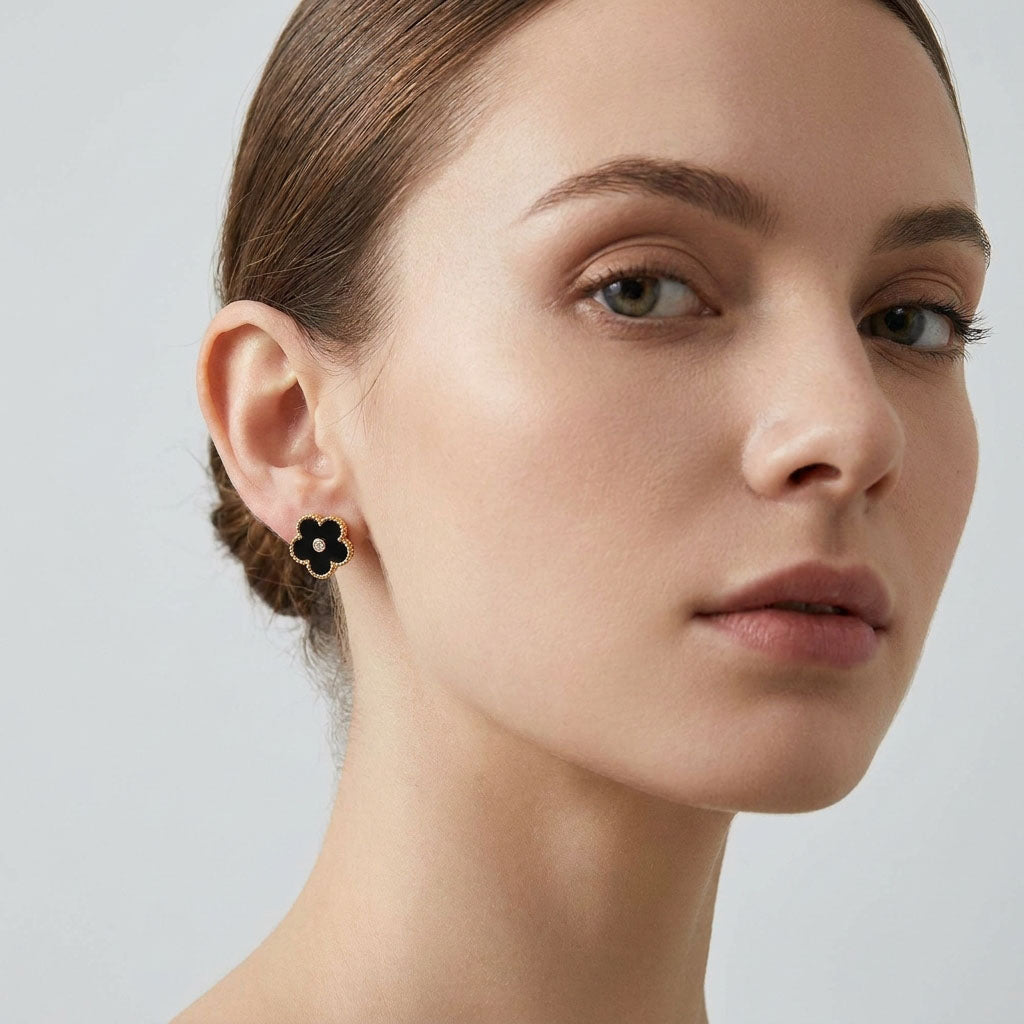 Black enamel flower earring with a beaded gold-tone rim on a model's ear