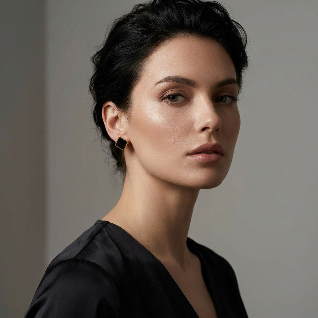 Dark-haired woman in a black blouse wearing a square black enamel stud