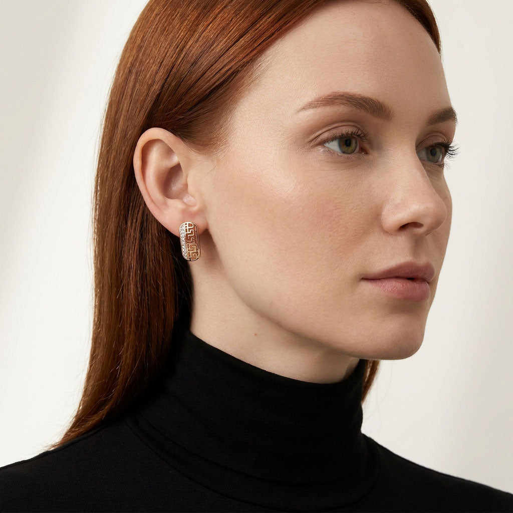 Red-haired model in a black polo neck wearing a gold-tone Greek key earring