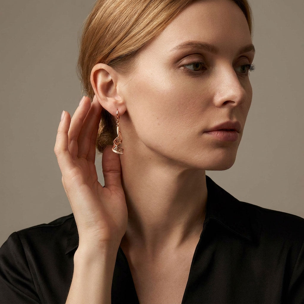 Model wearing a long gold-tone Greek pattern earring on a dark background