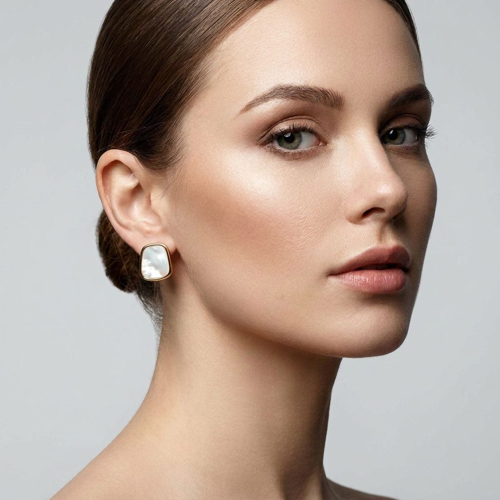 Model wearing gold-tone earrings with a pearly white inlay on the earlobe