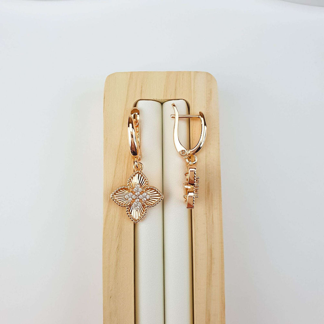 Gold-plated four-leaf clover earrings on a wooden stand, leverback clasp seen from the side