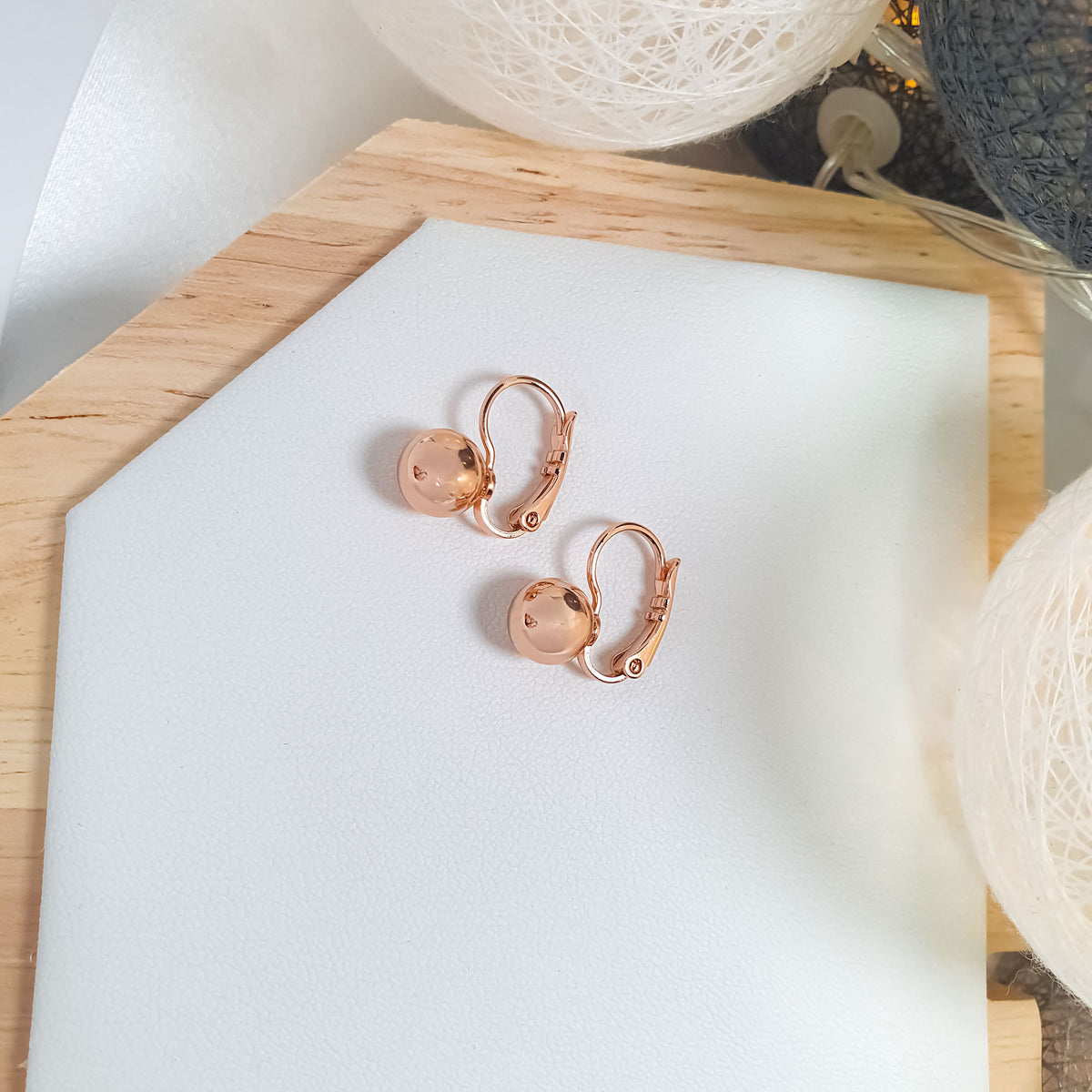 Gold-plated ball earrings on a white leather tray with yarn balls behind