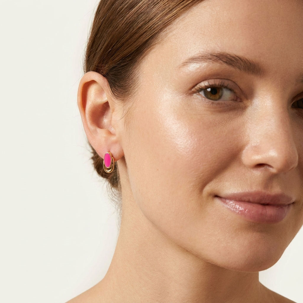 Bright pink oval earring on a gold-plated hoop in a woman's ear