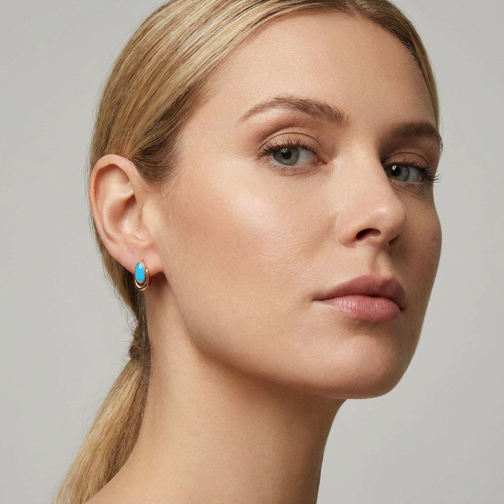 Sky-blue enamel earring with a gold-plated hoop in a fair-haired model's ear