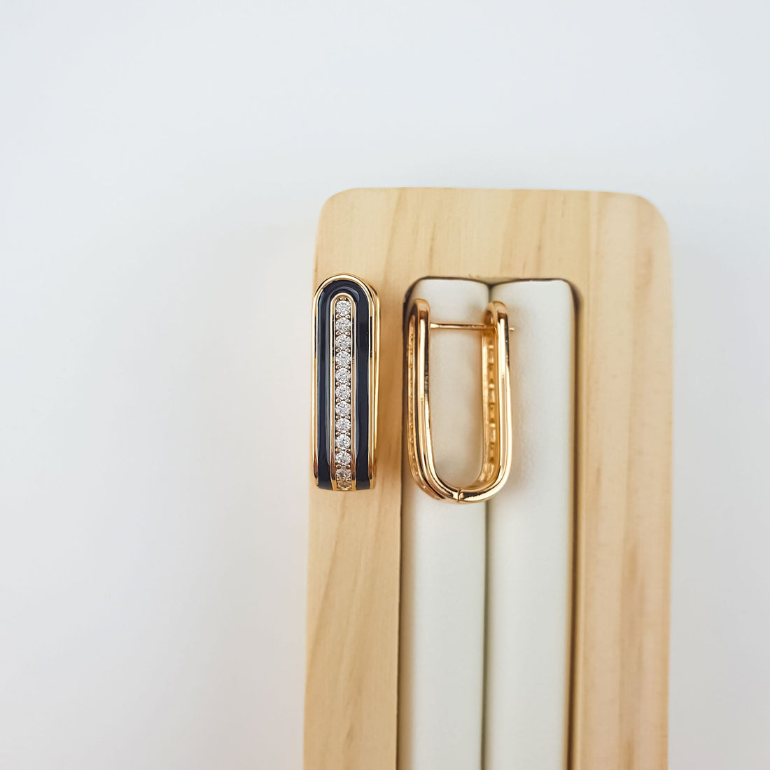 Black enamel earrings on a wooden stand with a smooth gold-plated back