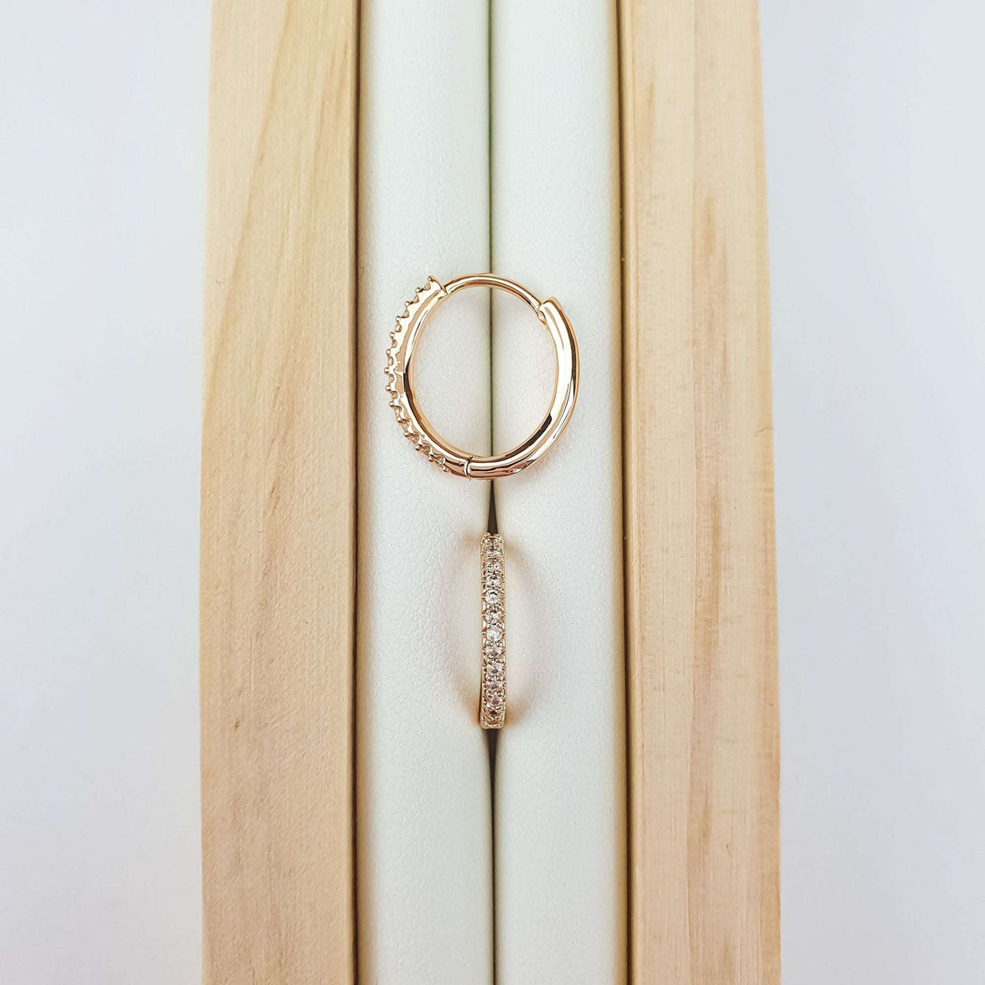 Rose gold-tone hoops on a wooden stand, close-up of the stones and clasp