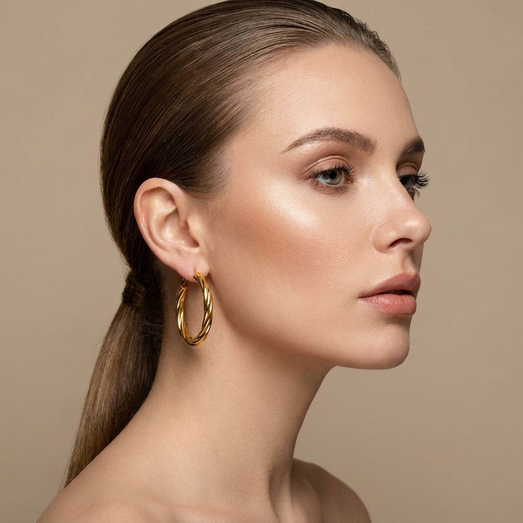Model in profile wearing a thick twisted gold-plated hoop, beige background