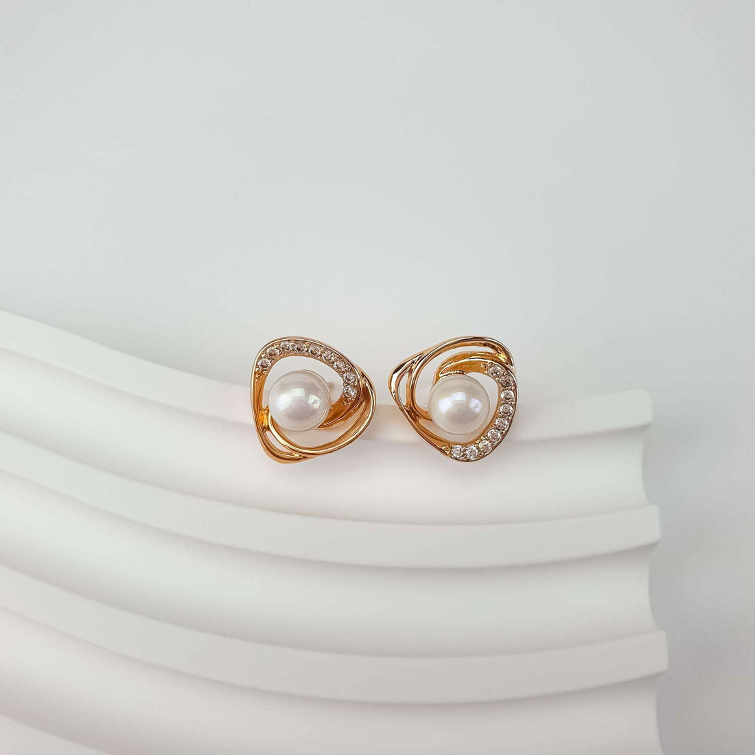 Faux pearl earrings at an angle, clasp visible, on a white wavy background