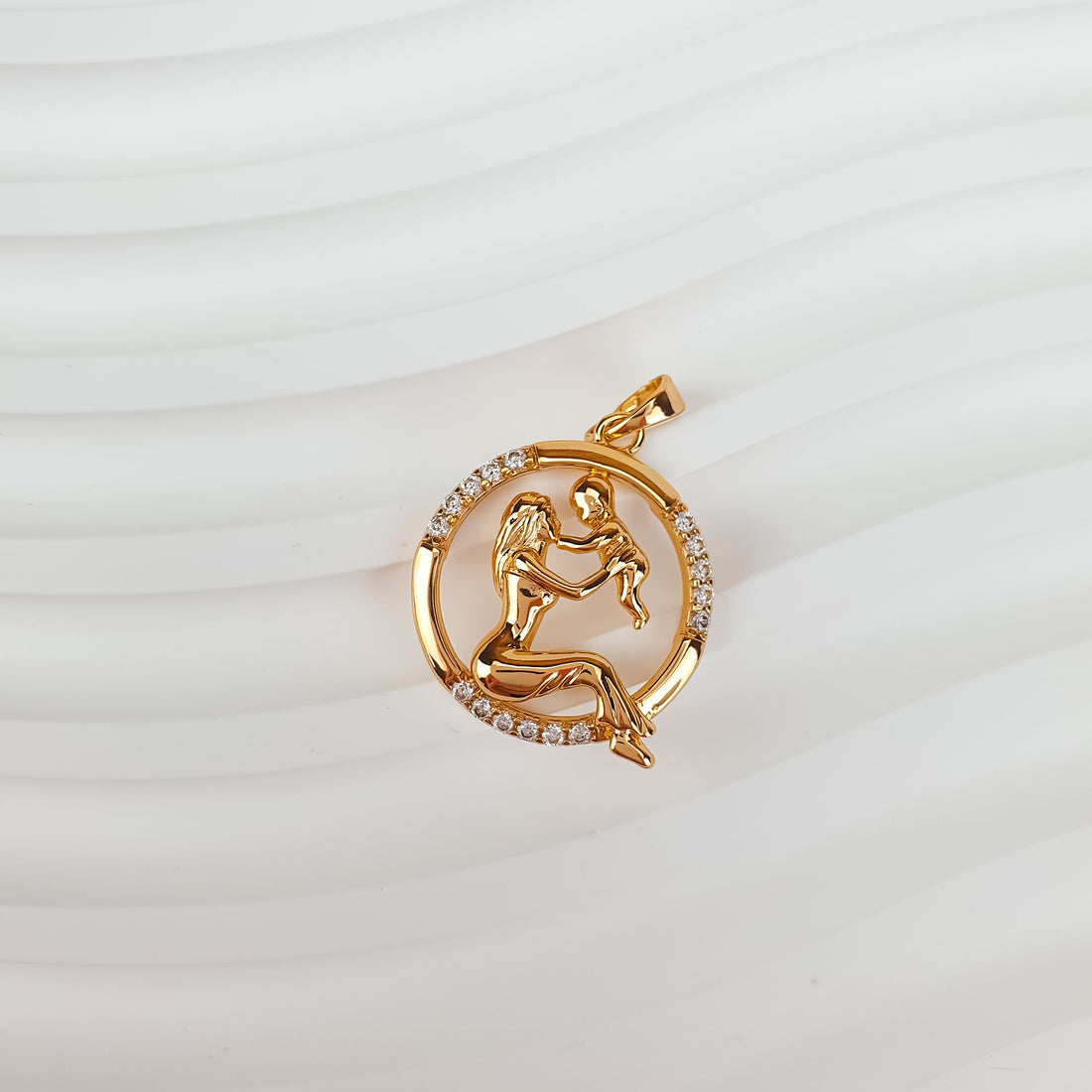 Gold-tone mother and child pendant at an angle on a wavy white background