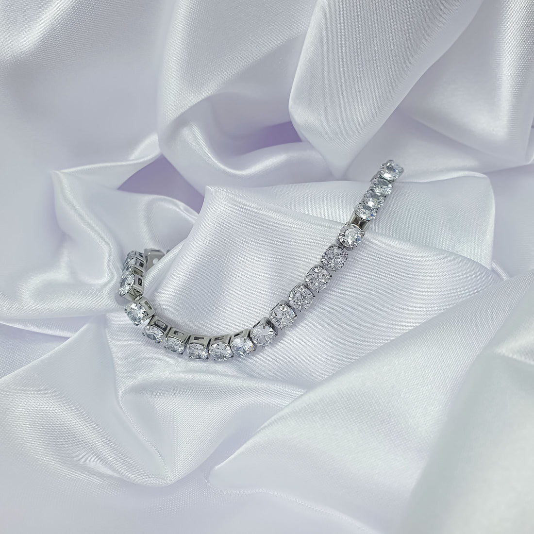 Silver-tone tennis bracelet draped over white satin, sparkling cubic zirconia