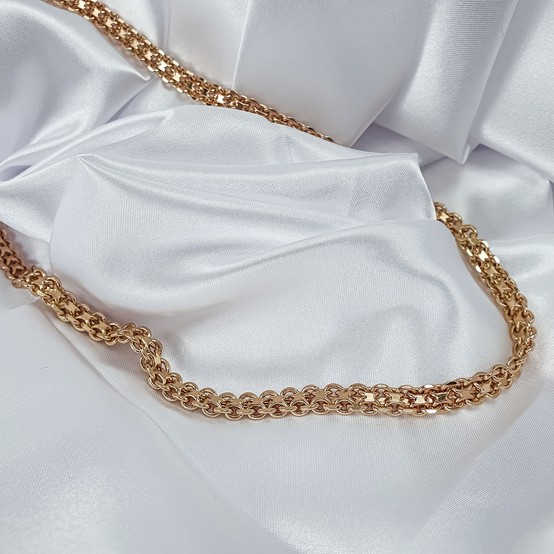 Gold-plated Bismarck chain necklace laid out in full on white satin