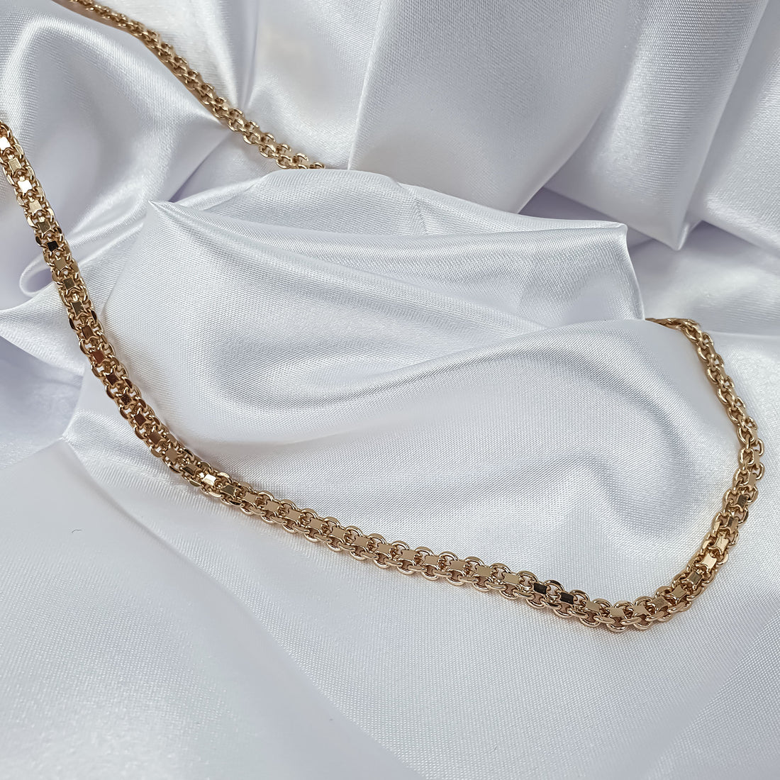 Gold-tone flat Bismarck chain laid out on white satin