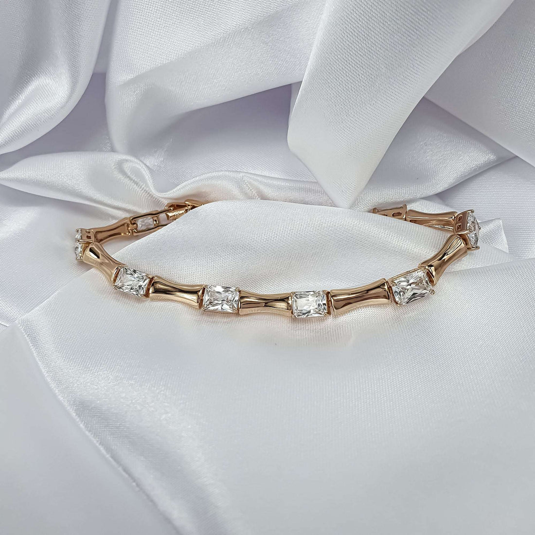 Gold-tone bamboo-style bracelet with clear stones on white satin