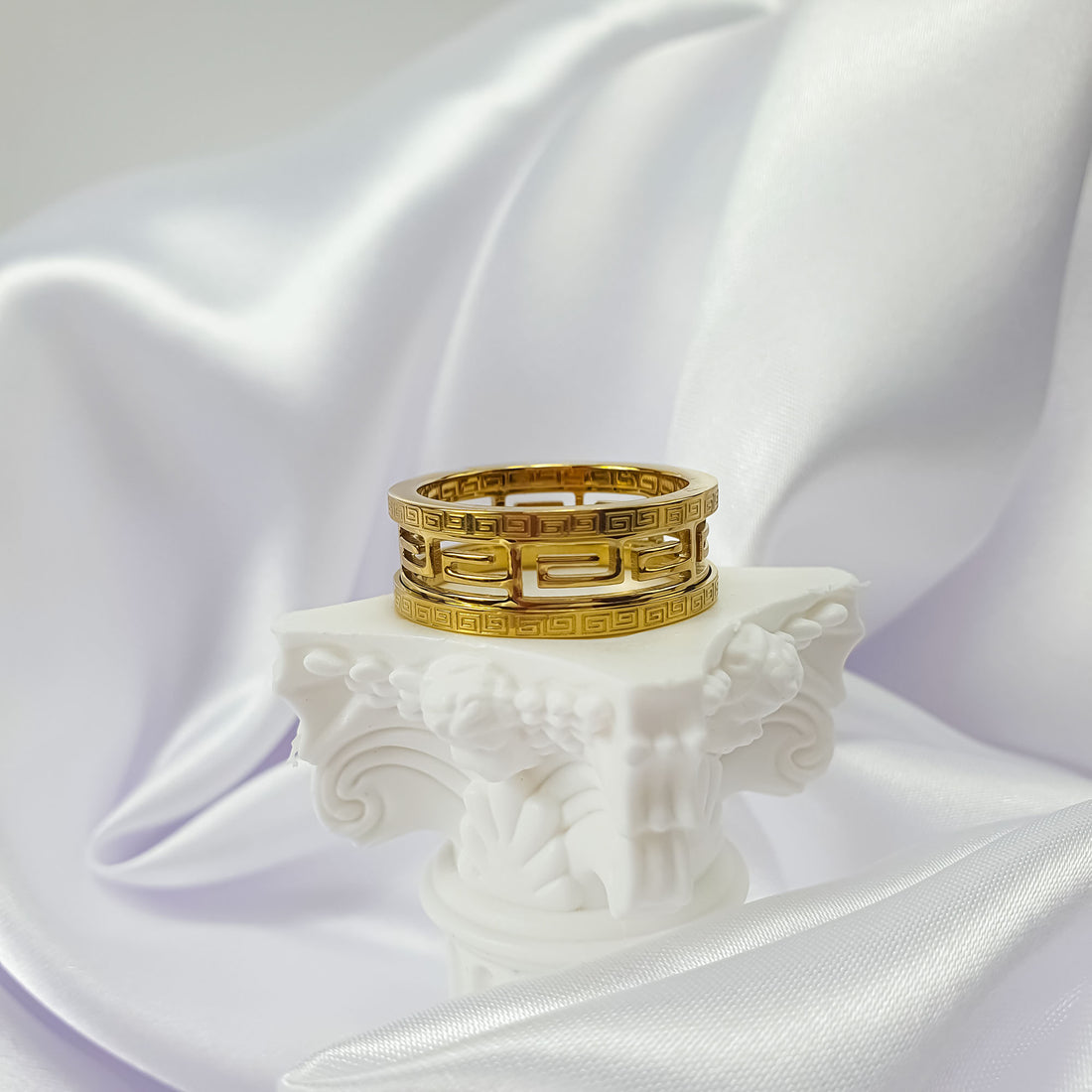 Gold-tone Greek meander ring with an openwork centre on a white column