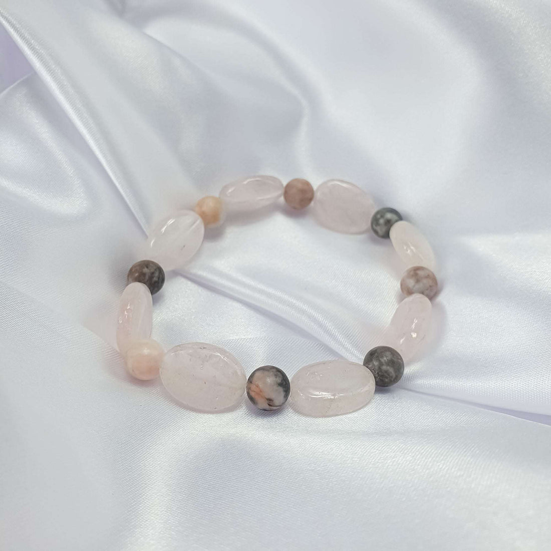 Soft-toned stone bracelet close-up on white silk, glossy beads